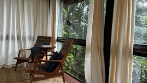 A room with a large window, wooden chairs, a small table, and a woven mat on the floor.