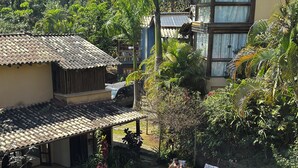 Ein Poolbereich mit Liegestühlen und einer Holzterrasse, umgeben von üppiger Vegetation und einem Gebäude mit Ziegeldach.