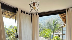 Ein blaugrünes Sofa mit weißer Decke und mehreren Kissen vor einem großen Fenster mit weißen Vorhängen.