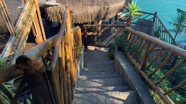 Eine Holztreppe führt zu einem Gebäude mit einem Strohdach am Ufer.