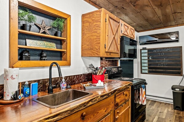 A kitchen with wooden cabinets, a black stove, and a wooden countertop. There is a sign on the wall and a window with plants.