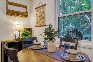 A dining area with a wooden table, chairs, a vase with greenery, a framed butterfly artwork, and a window with a forest view. - NEW Listing 🔥 Hot Tub • Mountain View • Fire Pit • EV Charger (Sevierville)