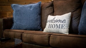 A brown leather sofa with two pillows, one blue and one white with "welcome HOME" text. - NEW Listing 🔥 Hot Tub • Mountain View • Fire Pit • EV Charger (Sevierville)