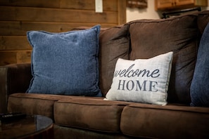 A brown leather sofa with two pillows, one blue and one white with "welcome HOME" text.