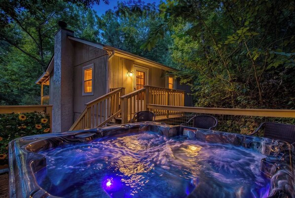 A wooden cabin with a hot tub and a deck, surrounded by trees.
