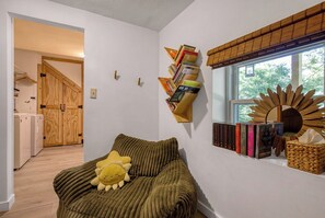 A room with a green sofa, a yellow plush toy, a wall-mounted bookshelf, and a window with a sunburst decoration. - NEW Listing 🔥 Hot Tub • Mountain View • Fire Pit • EV Charger (Sevierville)