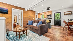 Un salon chaleureux avec un plancher en bois, un canapé en cuir marron, une table basse en bois et un tapis bleu à motifs.