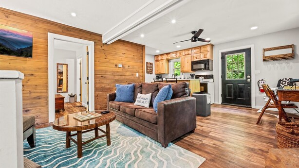 A cozy living room with a wooden floor, a brown leather sofa, a wooden coffee table, and a blue patterned rug. - NEW Listing 🔥 Hot Tub • Mountain View • Fire Pit • EV Charger (Sevierville)