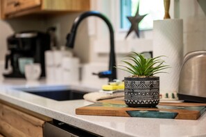 A kitchen counter with a coffee maker, a sink, and a potted plant on a wooden board.