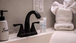 A bathroom sink with a black faucet, a soap dispenser, and a towel. - NEW Listing 🔥 Hot Tub • Mountain View • Fire Pit • EV Charger (Sevierville)