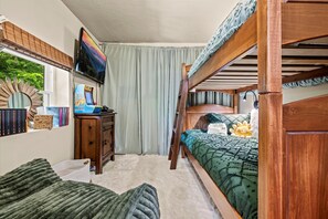 A bunk bed room with a television, books, and a window with curtains. - NEW Listing 🔥 Hot Tub • Mountain View • Fire Pit • EV Charger (Sevierville)