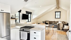 A modern kitchen with a built-in stove, oven, and refrigerator. There is a dining area with a table and chairs, and a living room with a sofa and a TV. - Newly built designer guesthouse nestled in Santa Barbara’s Sycamore Canyon. (Santa Barbara)