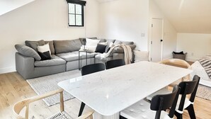A modern loft with a dining area, a gray sectional sofa, and a large window. - Newly built designer guesthouse nestled in Santa Barbara’s Sycamore Canyon. (Santa Barbara)
