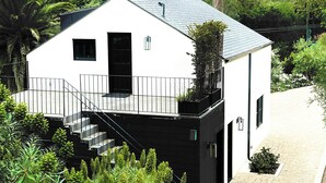A modern two-story house with a black exterior, white walls, and a grey roof. It features a staircase leading to a balcony with a metal railing. - Newly built designer guesthouse nestled in Santa Barbara’s Sycamore Canyon. (Santa Barbara)