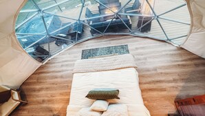 Ein mit Zeltdach versehenes Zimmer mit Bett, kleinem Tisch und Ausblick nach draußen durch eine Glaskuppel.