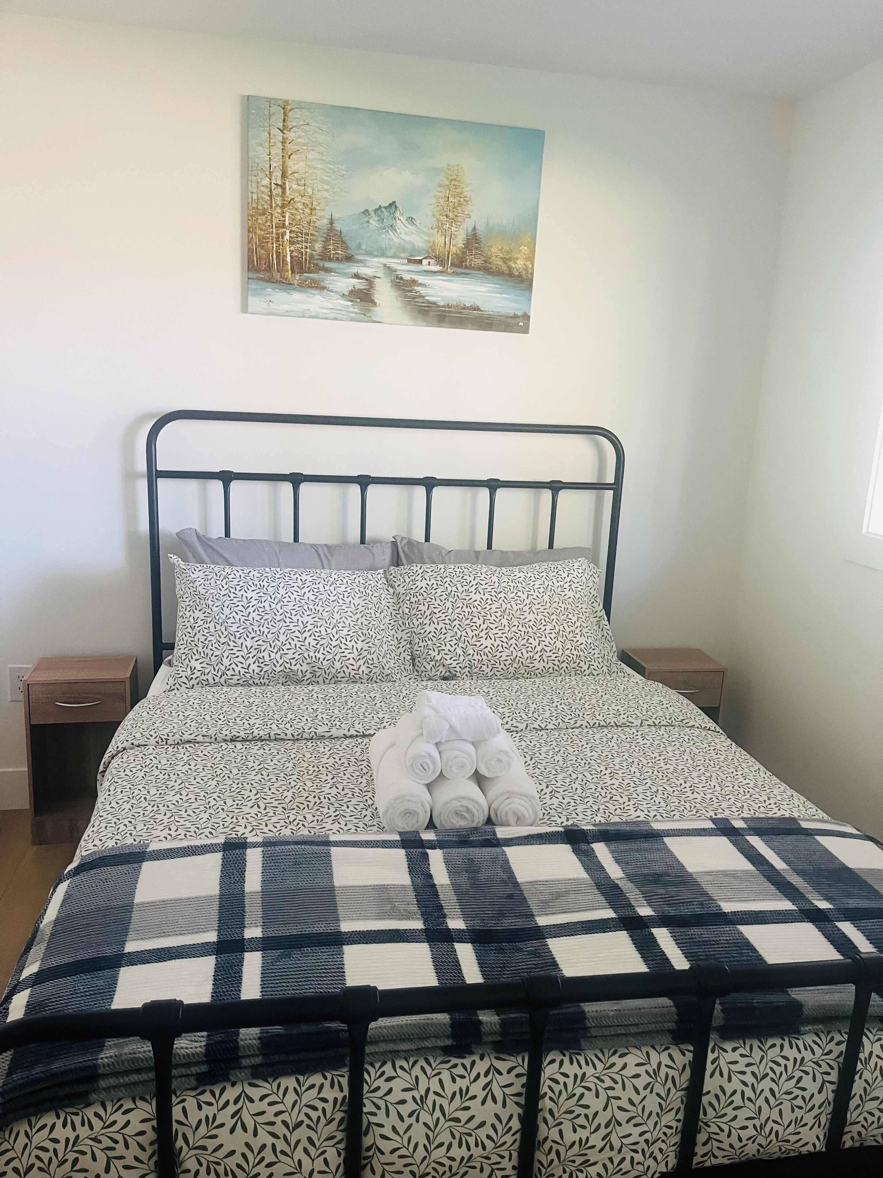 Ein Bett mit Metallgestell, gemusterten Betttextilien und einem Bild darüber.