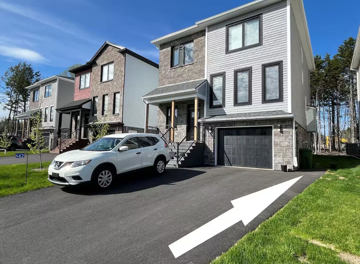 A modern two-story house with a white car parked in the driveway.