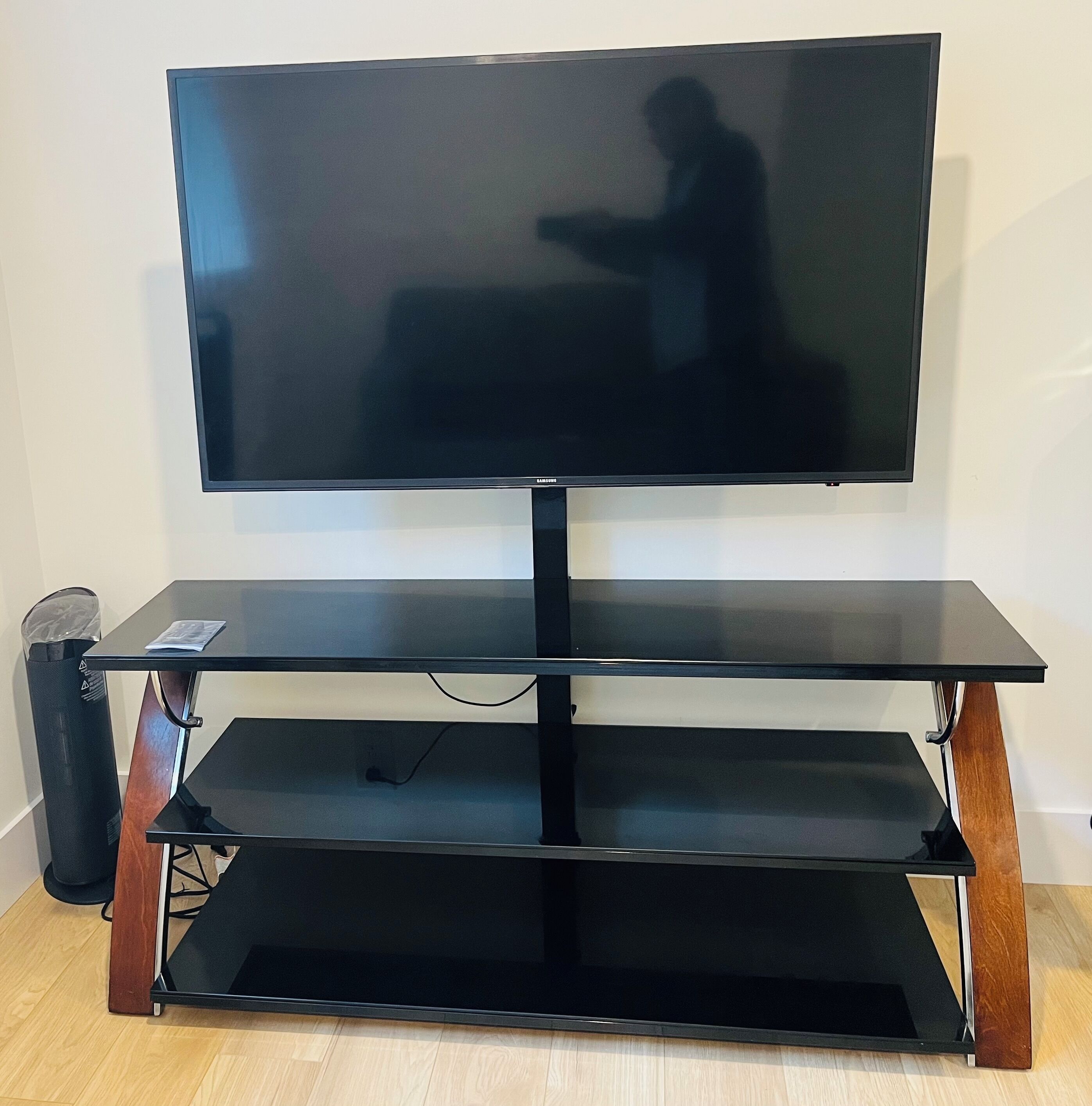 A flat-screen TV on a black stand with a wooden base and a shelf below.