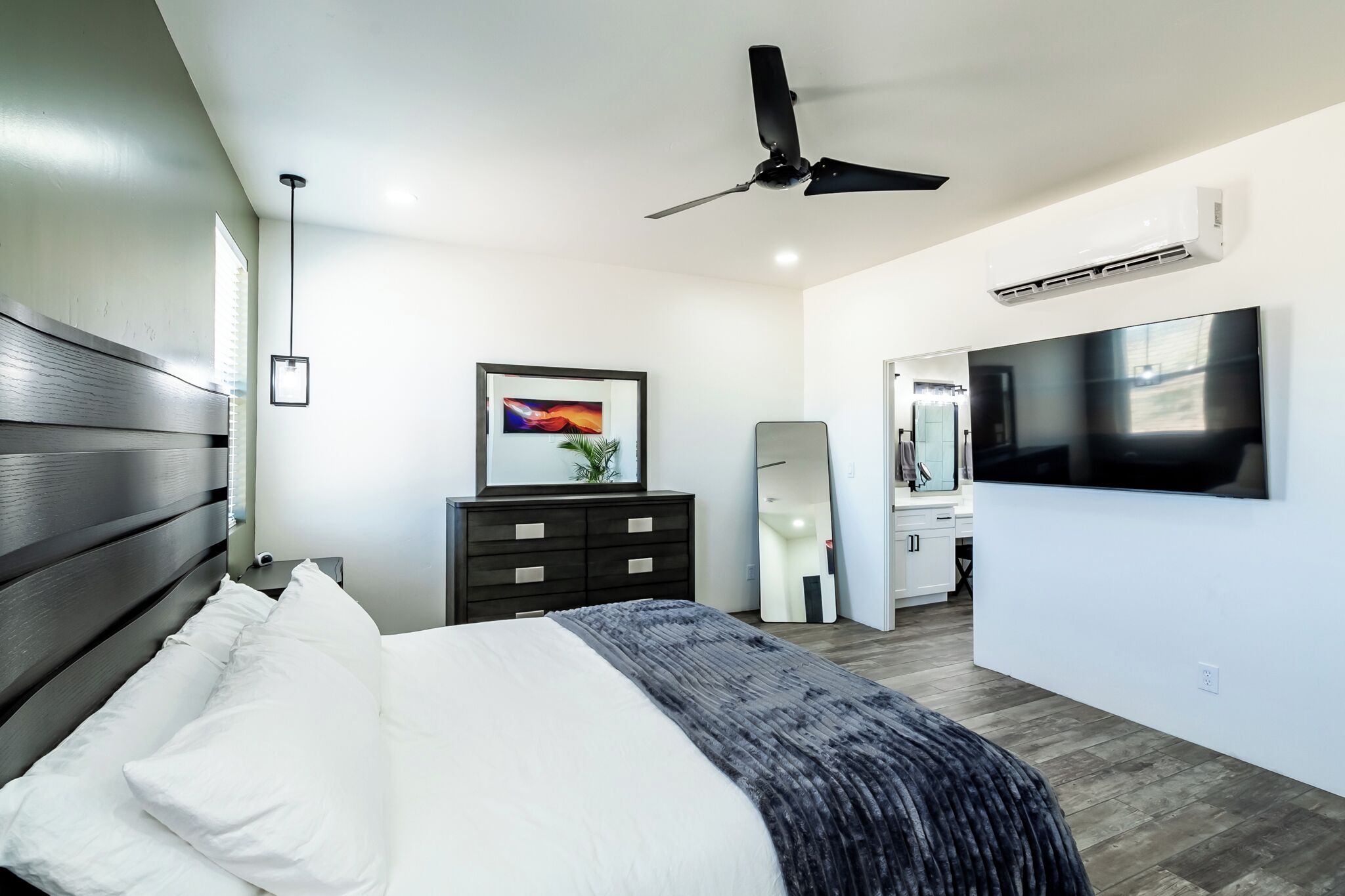 Un dormitorio moderno con cama, ventilador de techo, televisor, cómoda y espejo.