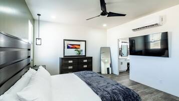 Un dormitorio moderno con cama, ventilador de techo, televisor, cómoda y espejo.