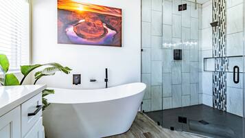 A modern bathroom with a freestanding bathtub, a glass-enclosed shower, and a large window.