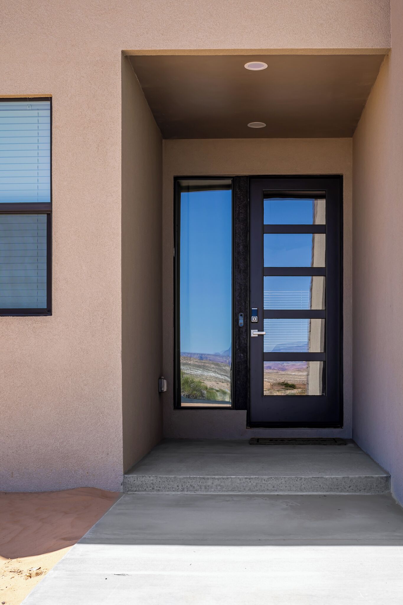 Une entrée moderne avec une porte en verre, un seuil en béton et une vue sur le paysage.