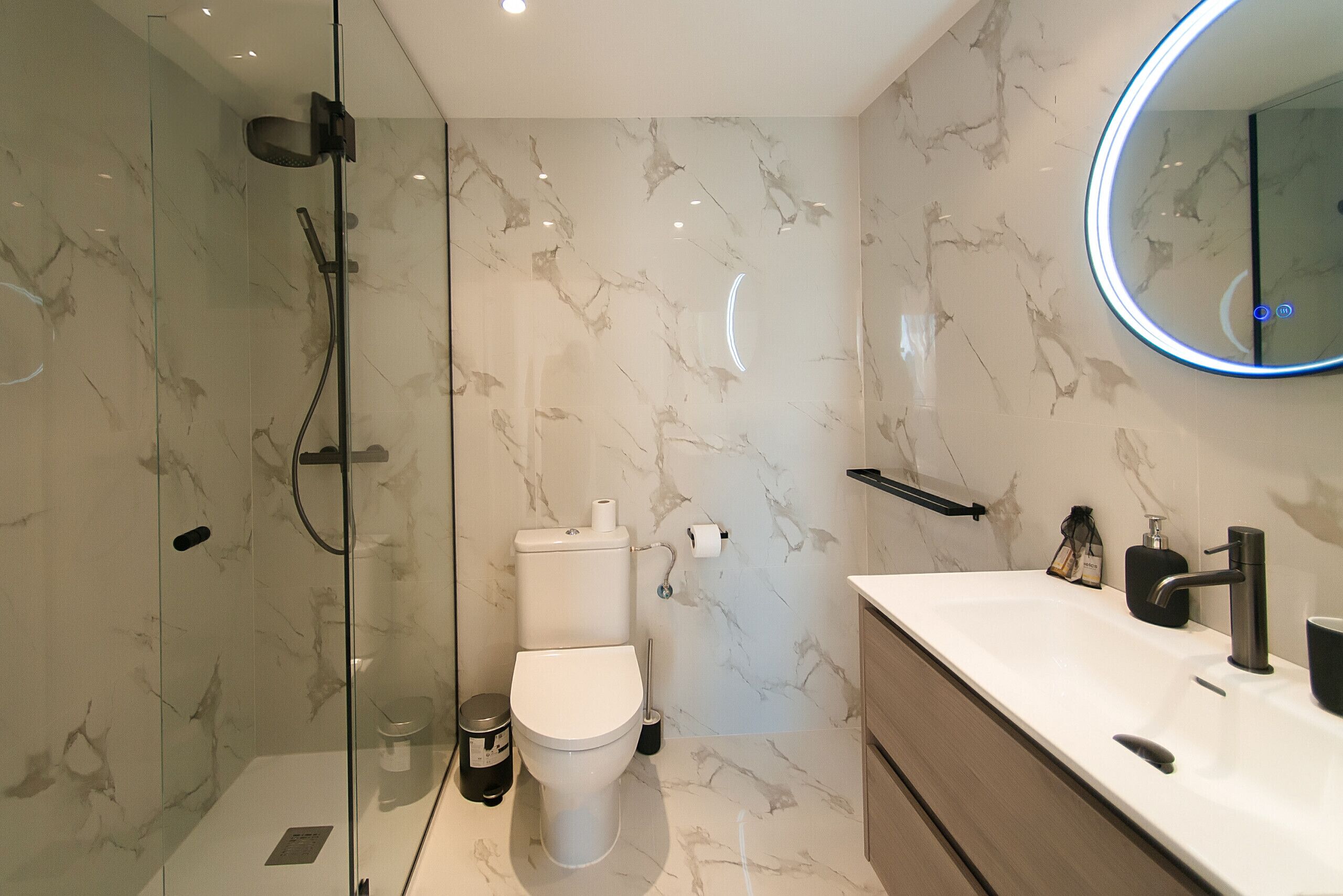 Un baño moderno con ducha envuelta en vidrio, inodoro y tocador con lavabo y espejo.