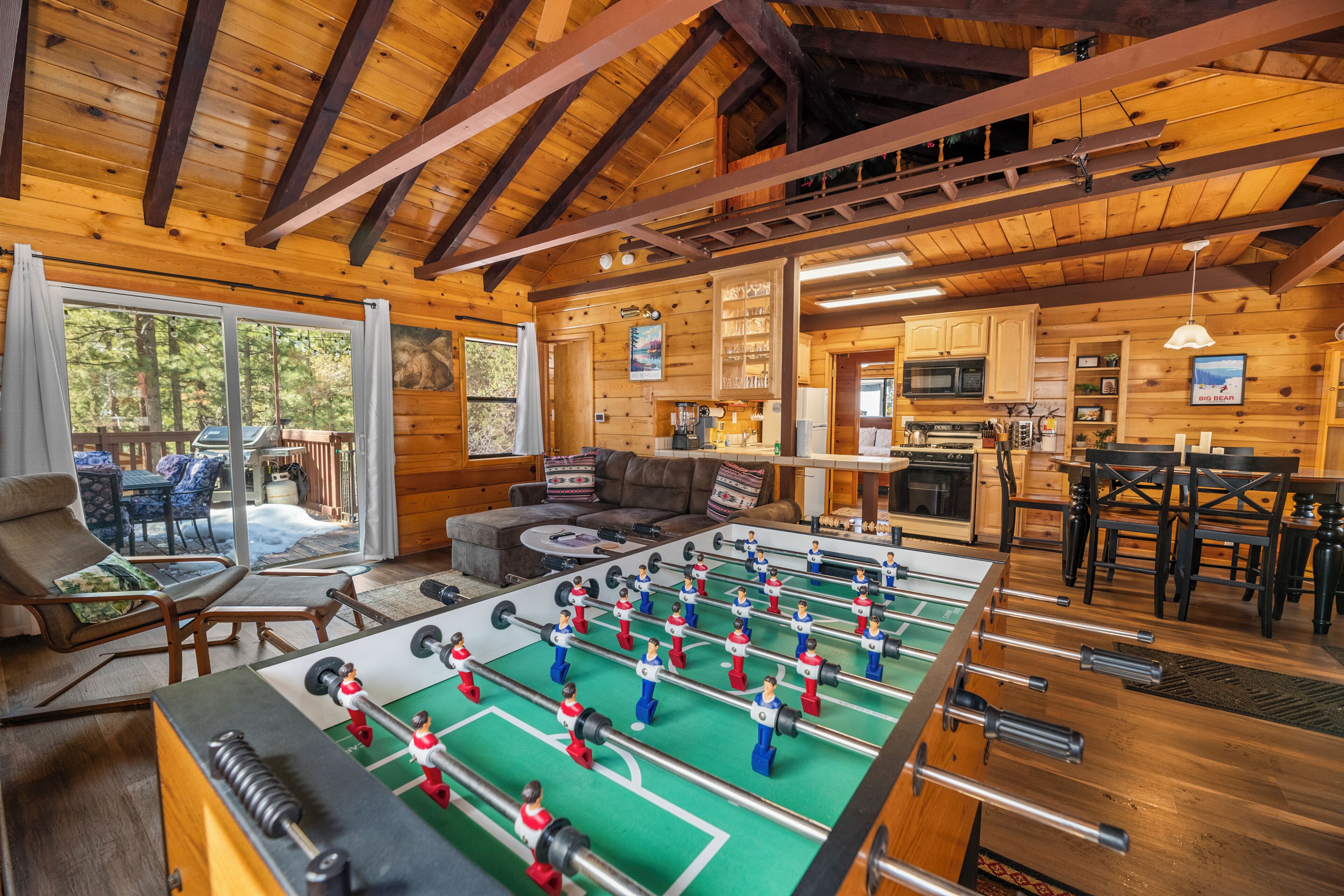 A cozy wooden interior with a foosball table, a kitchen, and a seating area with a view of the outdoors.