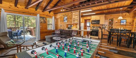 A cozy wooden interior with a foosball table, a kitchen, and a seating area with a view of the outdoors.