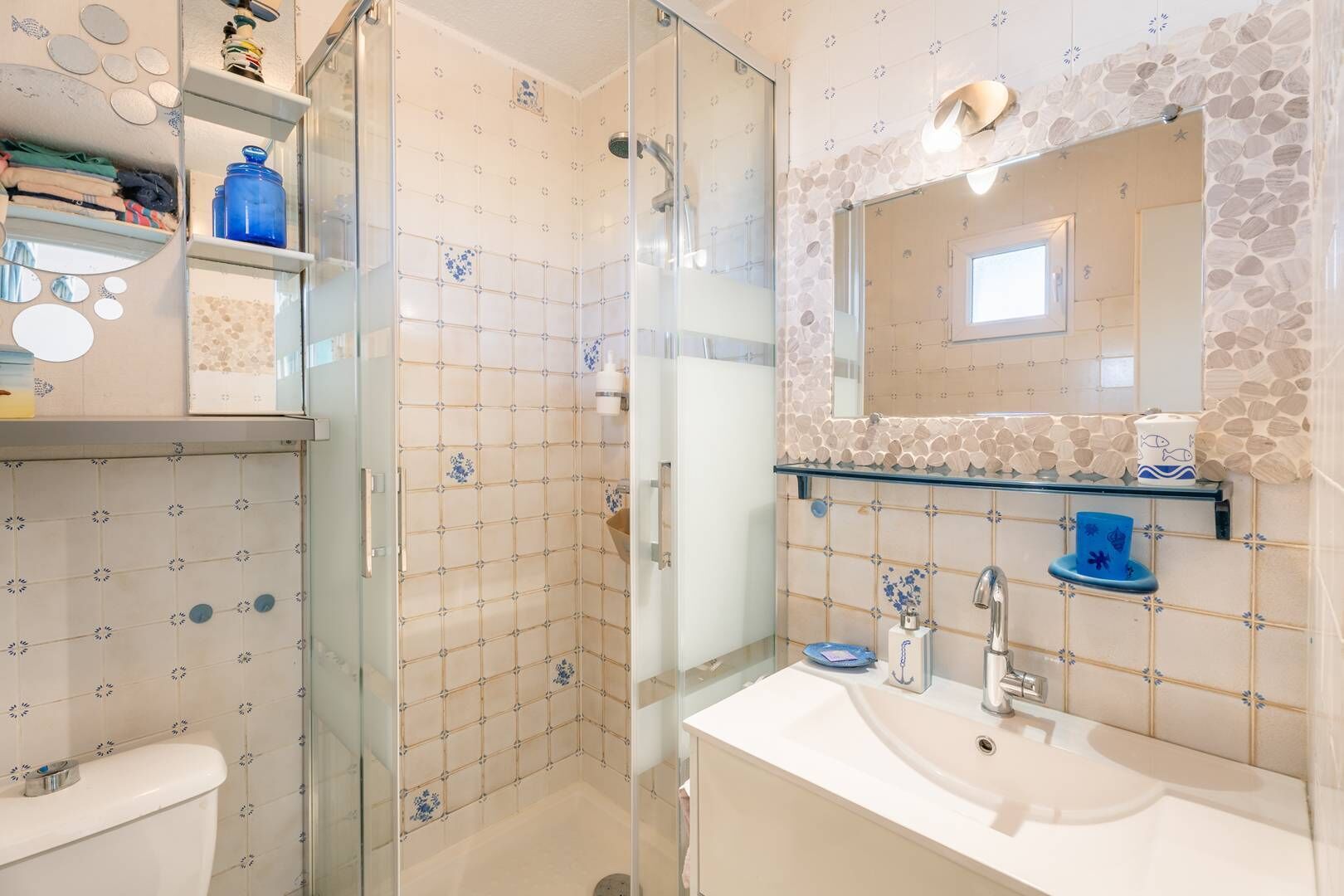 A bathroom with a glass shower enclosure, a white sink, and a mirror with a stone backsplash.
