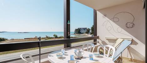 A balcony with a table set for two, overlooking a beach and the sea.