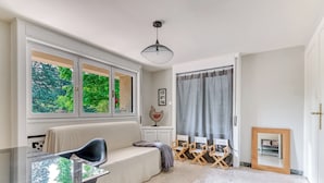 Un salon moderne avec une table en verre, un canapé et une vue sur la verdure grâce à de grandes fenêtres.