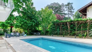 Une piscine rectangulaire avec une terrasse carrelée, entourée d’une végétation luxuriante et agrémentée d’une pergola.