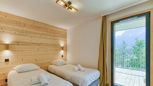 A hotel room with two beds, wooden paneling on the walls, a large window with a view of mountains, and a balcony.