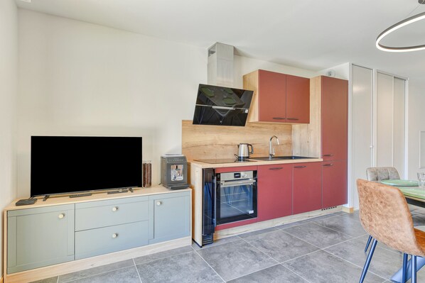 Una cocina moderna con horno empotrado, cafetera y televisor de pantalla plana sobre un mueble.