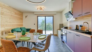A modern kitchen with a dining area, featuring a large window, wooden paneling, and a view of greenery.