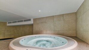 A hot tub in a modern bathroom with beige tiles and a recessed ceiling light.