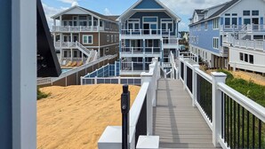 A beachfront property with multiple-story buildings, a wooden deck, and a sandy beach. - 5389- Heavenly Sunrise - Oceanfront Estate for 32 | Pool & Theater (Kill Devil Hills)