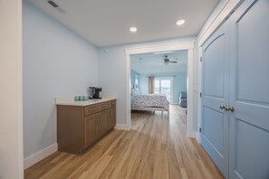 A hallway with a kitchen area, a bedroom with a bed and a window, and a door leading to another room. - 5389- Heavenly Sunrise - Oceanfront Estate for 32 | Pool & Theater (Kill Devil Hills)