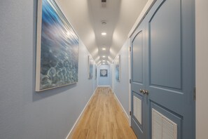 A hallway with a wooden floor, light blue walls, and doors with vents. - 5389- Heavenly Sunrise - Oceanfront Estate for 32 | Pool & Theater (Kill Devil Hills)