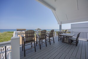 Um deck de madeira com móveis para área externa, vista para o oceano e um edifício ao fundo.