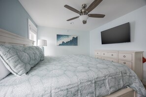 Ein Schlafzimmer mit einem Bett, einem Deckenventilator, einem an der Wand montierten Fernseher und einem Bild an der Wand.