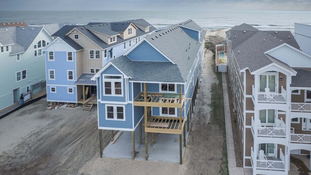 A beachfront property with multiple buildings, including a blue house with a balcony and a white building with a balcony. - 5389- Heavenly Sunrise - Oceanfront Estate for 32 | Pool & Theater (Kill Devil Hills)
