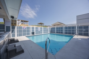 Una piscina con un puesto de salvavidas, sillas de descanso y una zona cubierta con techo.