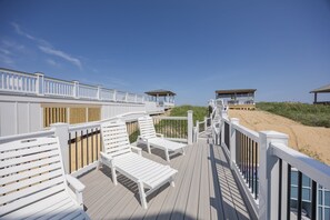 A wooden deck with white railings and benches, overlooking a sandy beach.