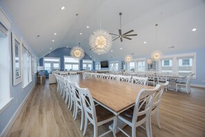 A spacious kitchen with a large wooden table surrounded by white chairs, modern pendant lights, and a ceiling fan. - 5389- Heavenly Sunrise - Oceanfront Estate for 32 | Pool & Theater (Kill Devil Hills)
