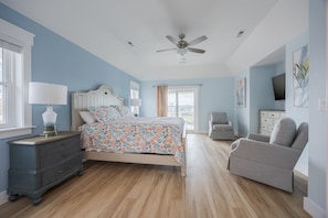 A bedroom with a bed, a dresser, a chair, a ceiling fan, and artwork on the walls.