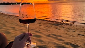 A person holding a wine glass on a beach with a sunset in the background. - Romantic Beachfront Retreat - Everything You Want, In Las Terrenas - 2 Rooms (Las Terrenas)