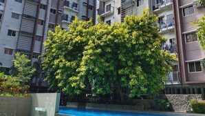 A multi-story residential building with balconies, a swimming pool, and lush greenery.