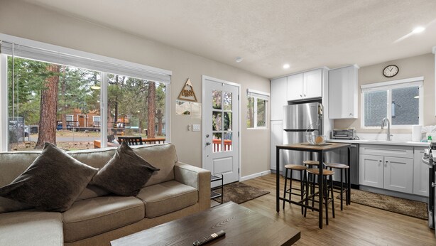 A modern living room with a sofa, coffee table, and kitchen area including a refrigerator, stove, and bar stools. - The Maple Lane Hideaway (Sugarloaf)